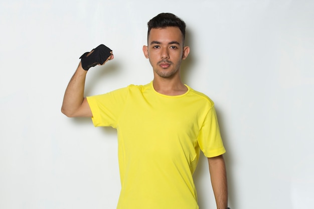 Jovem desportivo vestido com uma camiseta amarela, mostrando um gesto forte no fundo branco