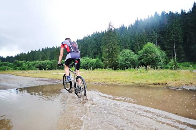 jovem dirigindo mountain bike sobre o rio de água