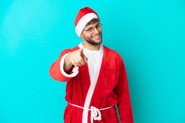 Jovem disfarçado de papai noel isolado em um fundo azul apontando o dedo para você com uma expressão confiante