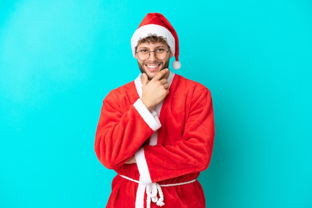 Jovem disfarçado de Papai Noel isolado em um fundo azul com óculos e sorrindo