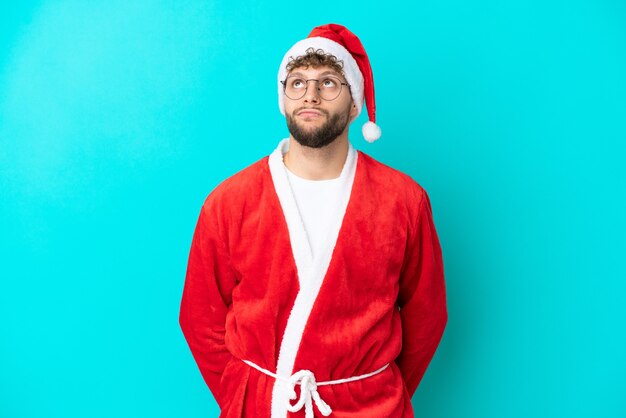 Jovem disfarçado de Papai Noel isolado em um fundo azul olhando para cima