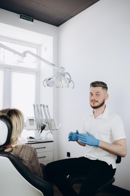 Jovem divertido ortodontista dentista caucasiano homem vestindo vestido mostrando dentes de mordida de mandíbula para paciente mulher sentada na cadeira de escritório do dentista armário interno perto de estomatologista Tratamento de esmalte de saúde