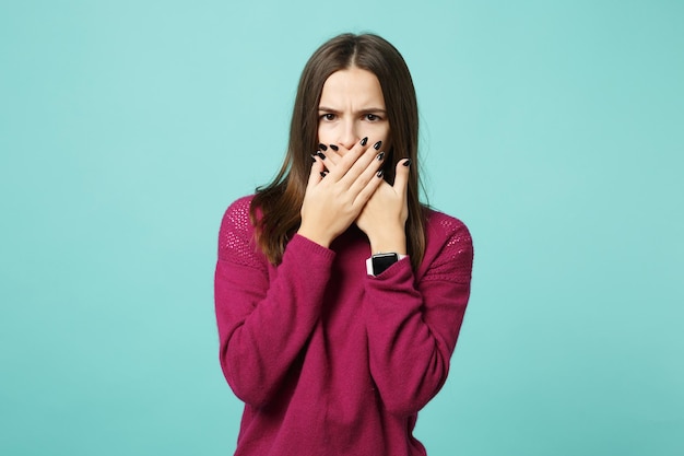 Jovem divertido triste chateado perplexo perturbar menina mulher morena posando cobrir a boca com as mãos isoladas no retrato de estúdio de fundo de parede azul. Conceito de estilo de vida de emoções sinceras de pessoas. Mock up espaço de cópia.