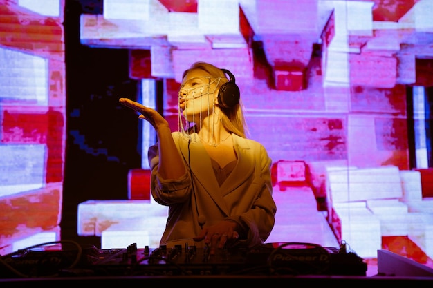 Jovem DJ feminina em uma boate no console, a garota está vestindo um terno branco e joias no rosto