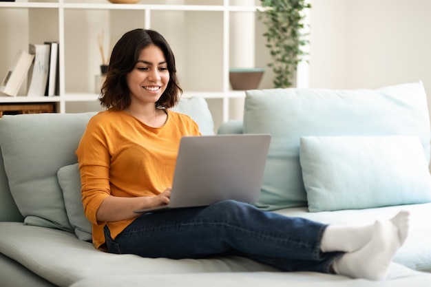 Jovem do Oriente Médio navegando na Internet no laptop enquanto relaxa em casa