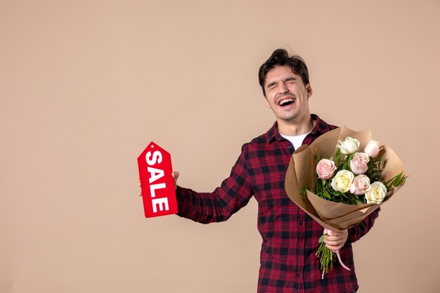 Jovem do sexo masculino segurando lindas flores e uma placa de identificação de venda na parede marrom.