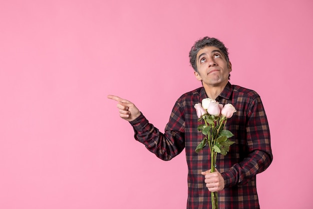 Jovem do sexo masculino segurando lindas rosas cor de rosa na parede rosa