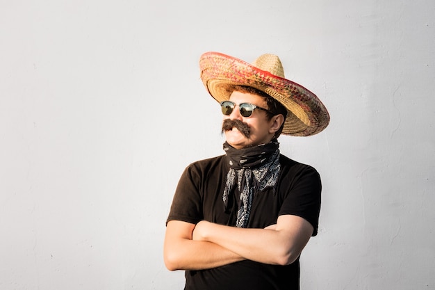 Jovem do sexo masculino vestido com sombrero mexicano tradicional, bigode falso, bandana e óculos escuros. Conceito festivo ou de halloween de homem se passando por bandido ou gangster de estilo ocidental