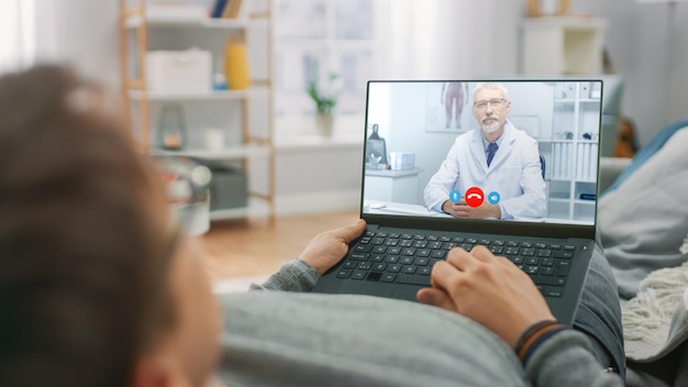 Jovem doente em casa usando computador portátil para falar com seu médico por videoconferência aplicativo médico Mulher verifica possíveis sintomas com médico profissional usando aplicativo de vídeo chat on-line