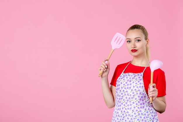 Jovem dona de casa segurando talheres na parede rosa de frente