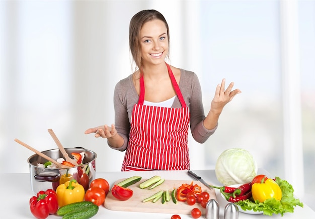 Jovem dona de casa sorridente em avental cozinhando comida saudável