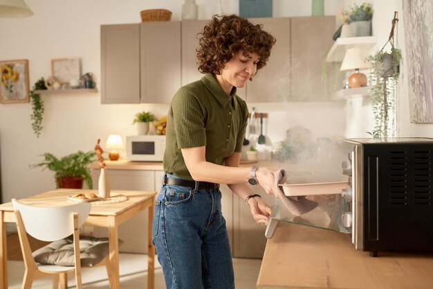 Foto jovem dona de casa tirando comida queimada do forno durante o cozimento na cozinha em casa