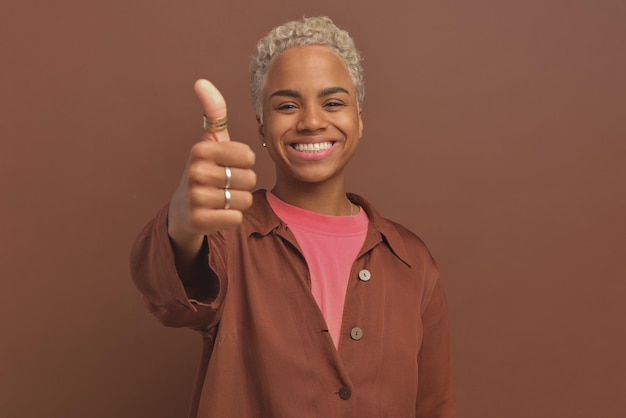 Jovem e alegre mulher afro-americana estende a mão para a câmera mostrando o polegar