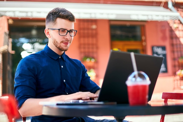 Jovem e atraente hipster freelancer trabalhando remotamente em laptop no café ao ar livre empresário navegando
