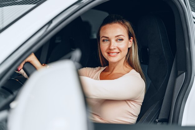 Jovem e atraente mulher caucasiana sentada em seu carro recém-comprado na concessionária