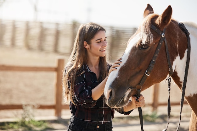 Jovem e atraente veterinária cuida de cavalo fofo acariciando seu h