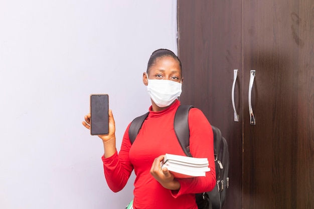 Jovem e bela aluna africana negra segurando uma tela de telefone e livros por outro lado