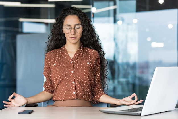 Jovem e bela desenvolvedora web hispânica trabalhando dentro de uma mulher de prédio de escritórios descansando meditando em