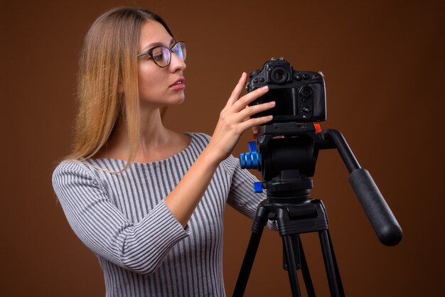 Jovem e bela fotógrafa verificando a câmera DSLR no tripé