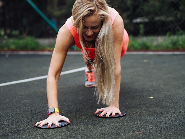 Jovem e bela loira fitness modelo com cabelo comprido em roupa ativa laranja neon fazendo exercícios no chão