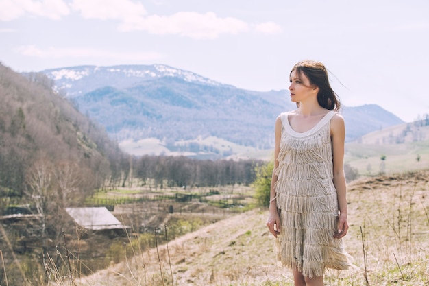 Foto jovem e bela modelo feminino em uma paisagem com montanhas e vilarejos, em uma colina.