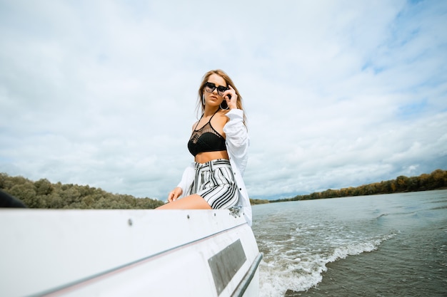 Jovem e bela modelo feminino no convés de um iate no mar. conceito de viagens e iatismo. viagem de luxo no iate. jovem mulher me divertindo no convés do barco navegando no mar.