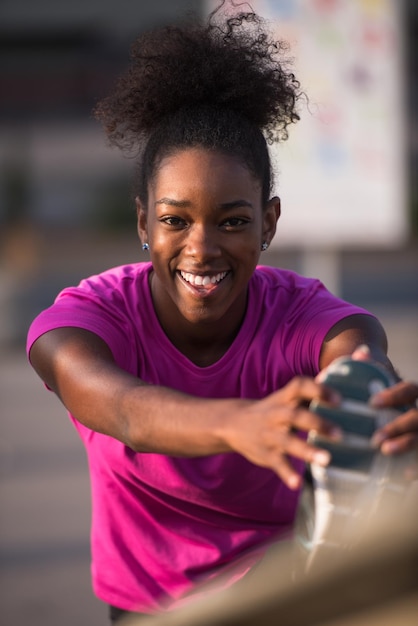 jovem e bela mulher afro-americana fazendo aquecimento e alongamento com a perna levantada para a ponte antes da corrida matinal com o nascer do sol ao fundo