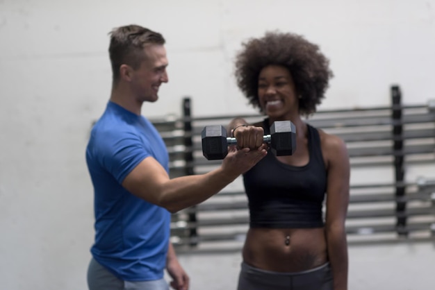 jovem e bela mulher afro-americana fazendo bíceps com instrutor de fitness em uma academia