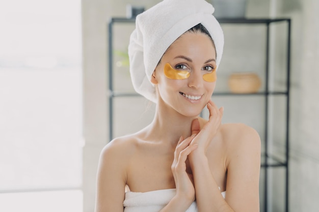 Jovem e bela mulher aplica tapa-olhos anti-rugas Garota feliz cuida do cabelo e do corpo