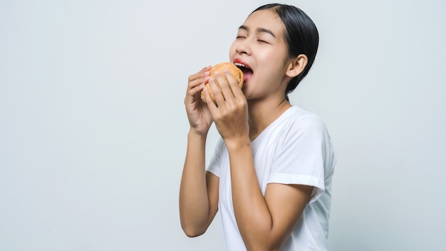 Jovem e bela mulher asiática comendo hambúrguer, sentindo-se feliz.