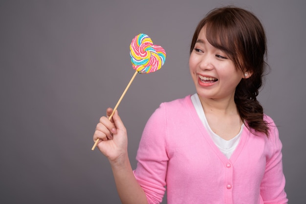 Jovem e bela mulher asiática segurando um pirulito colorido