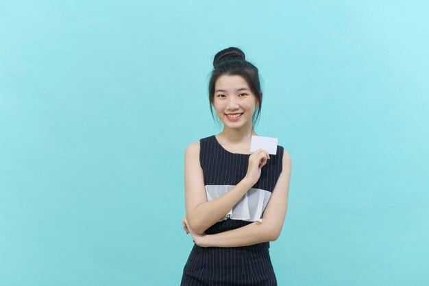 Jovem e bela mulher asiática sorrindo, mostrando, apresentando cartão de crédito para fazer o pagamento ou pagar negócios on-line sobre fundo azul