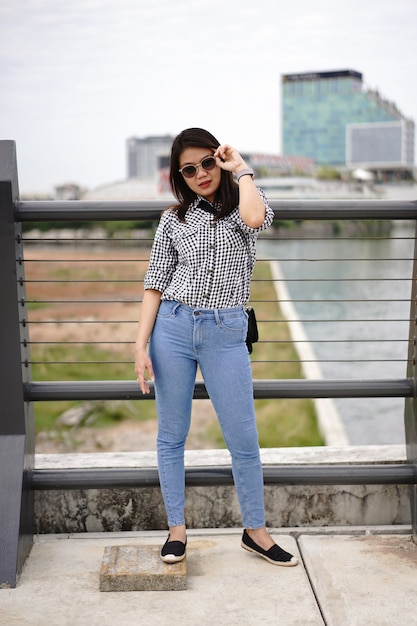 Jovem e bela mulher asiática vestindo camisa xadrez e jeans azul posando ao ar livre