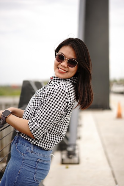 Jovem e bela mulher asiática vestindo camisa xadrez e jeans azul posando ao ar livre