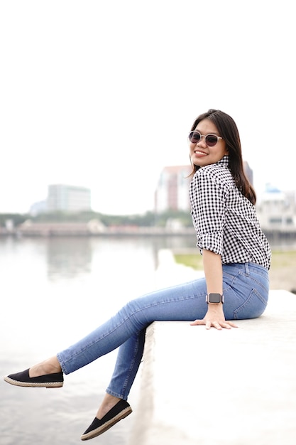 Jovem e bela mulher asiática vestindo camisa xadrez e jeans azul posando ao ar livre