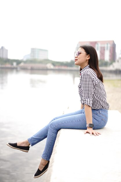 Jovem e bela mulher asiática vestindo camisa xadrez e jeans azul posando ao ar livre