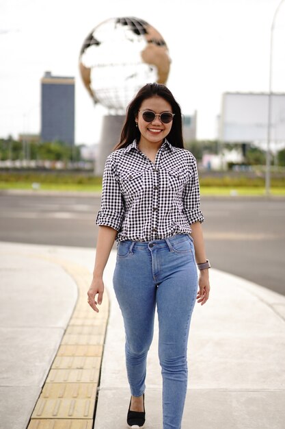 Jovem e bela mulher asiática vestindo camisa xadrez e jeans azul posando ao ar livre