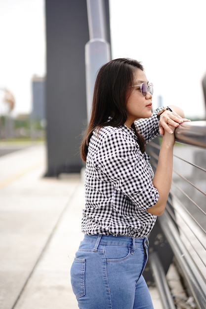 Jovem e bela mulher asiática vestindo camisa xadrez e jeans azul posando ao ar livre