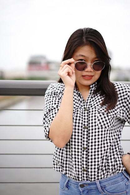Jovem e bela mulher asiática vestindo camisa xadrez e jeans azul posando ao ar livre