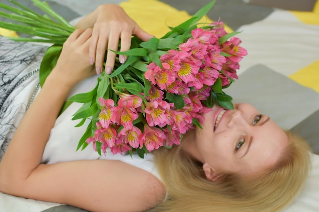 jovem e bela mulher encontra-se na cama com um buquê de flores frescas