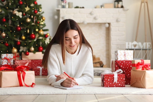 Jovem e bela mulher escrevendo uma lista de compras ou de desejos para o Natal em casa