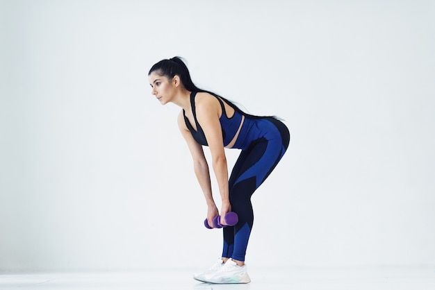 Jovem e bela mulher fazendo exercícios com halteres no estúdio de fitness