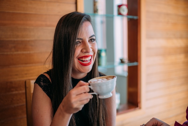 Jovem e bela mulher latina feliz tomando cappuccino em um café de rua