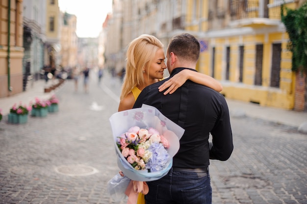 Jovem e bela mulher loira segurando um buquê de flores e abraçando um homem