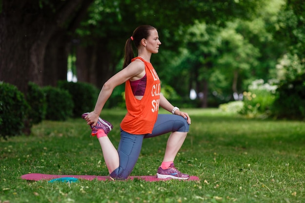 Jovem e bela mulher medita em um dia de verão no parque Ideia e conceito de calma em uma cidade movimentada e um estilo de vida saudável, estendendo-se e preparando-se para uma corrida no parque