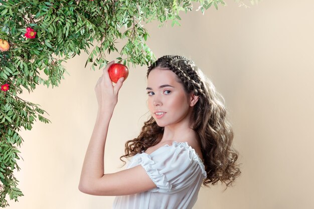 Jovem e bela mulher no jardim do Éden colhendo uma fruta madura