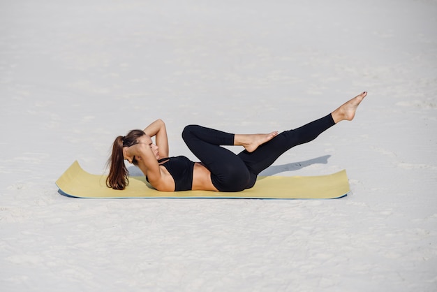 Jovem e bela mulher praticando ioga, fazendo flexões exercem-se na praia do mar. Yoga fitness e conceito de estilo de vida saudável. Mulher bonita em roupas esportivas, fazendo exercícios no tapete de ioga.