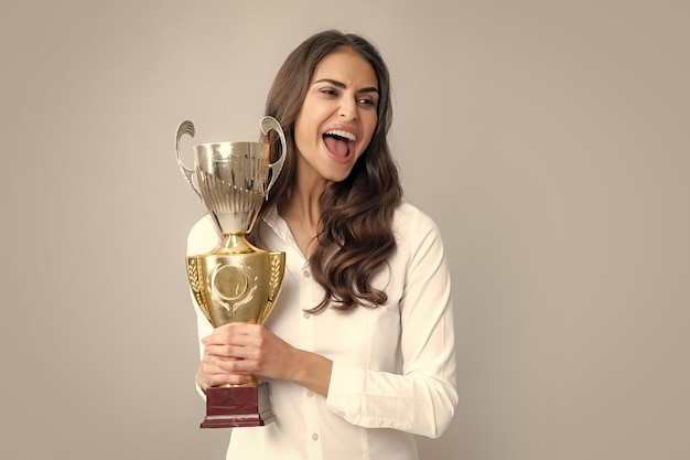 Jovem e bela mulher segurando o troféu sobre fundo cinza Mulher segurando um troféu Empregado de sucesso detém a taça do vencedor Cerimônia de premiação para o vencedor Melhor gerente