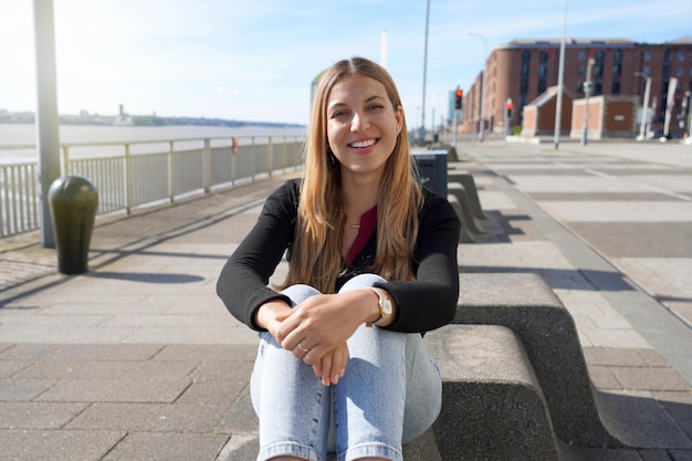 Jovem e bela mulher sentada relaxada à beira-mar de Liverpool em dia ensolarado na Inglaterra