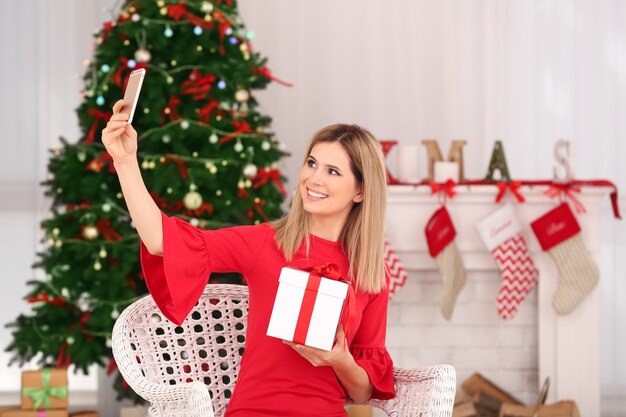 Jovem e bela mulher tirando selfie em um quarto decorado para o Natal